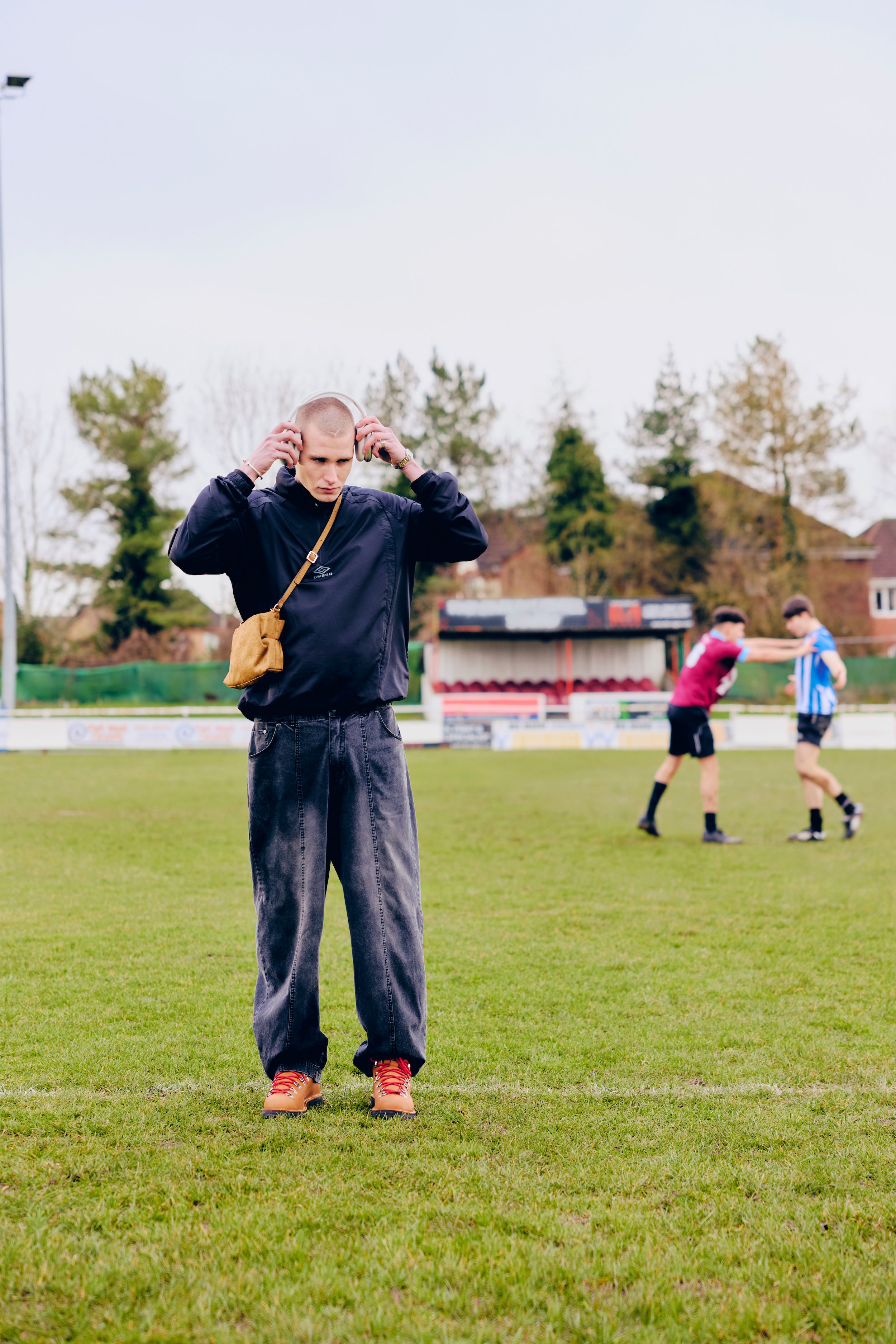 Person, wearing an Umbro hoodie, standing on a grassy field with two other people in the background